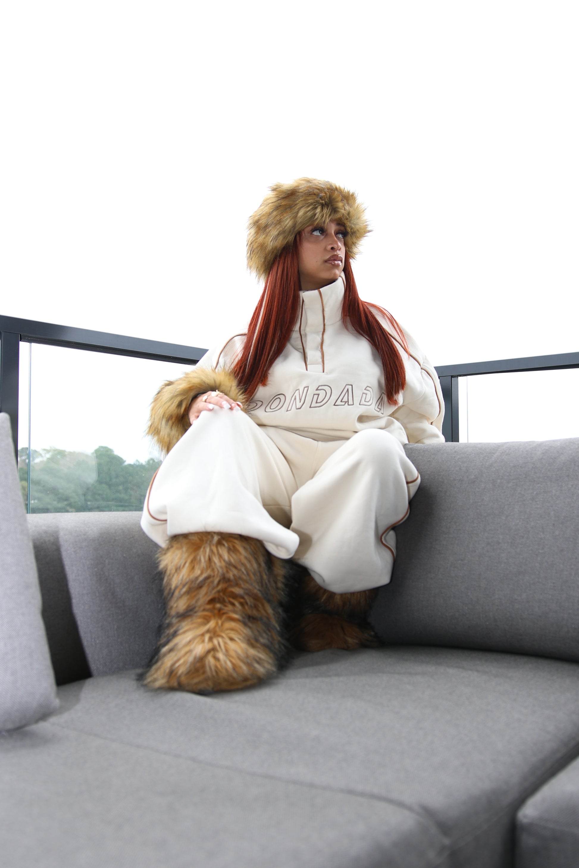 Person wearing a white hoodie with fur trim sitting on a gray couch.